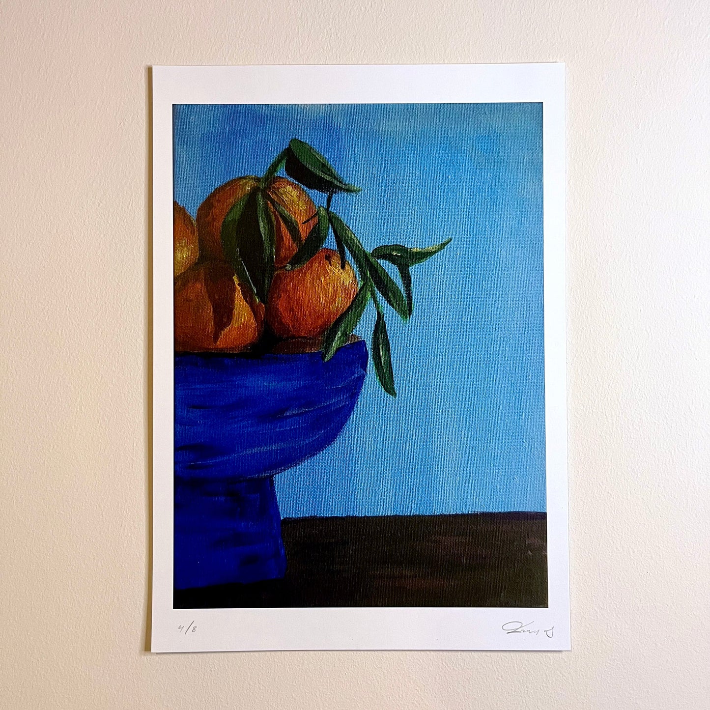 Art print of oranges in a blue bowl on a beige wall